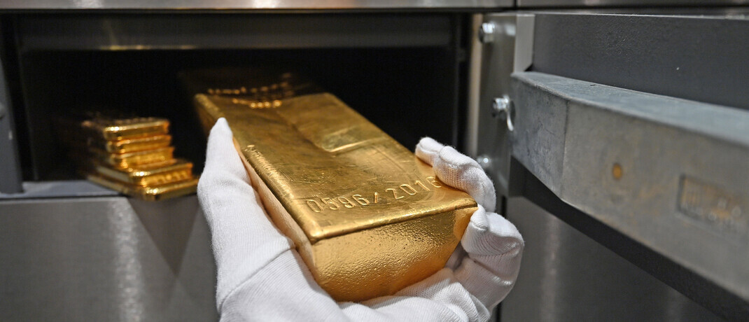 Ein Mann legt einen Goldbarren in den Tresor. 